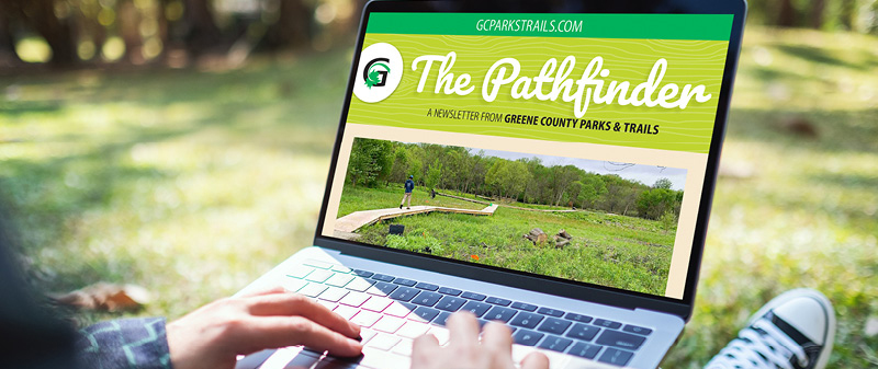Hands typing on a laptop showing The Pathfinder newsletter in the woods